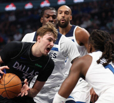 Cooper Flagg of the Dallas Mavericks drives against Ayo Dosunmu and Naz Reid of the Minnesota Timberwolves at American Airlines Center.