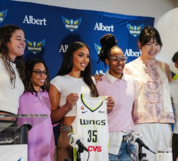 Azzi Fudd holds up her new #35 Dallas Wings jersey while posing with teammates Maddy Siegrist, JJ Quinerly, Grace Berger, Aziaha James, Li Yueru, and Shyanne Sellers at her introductory press conference.