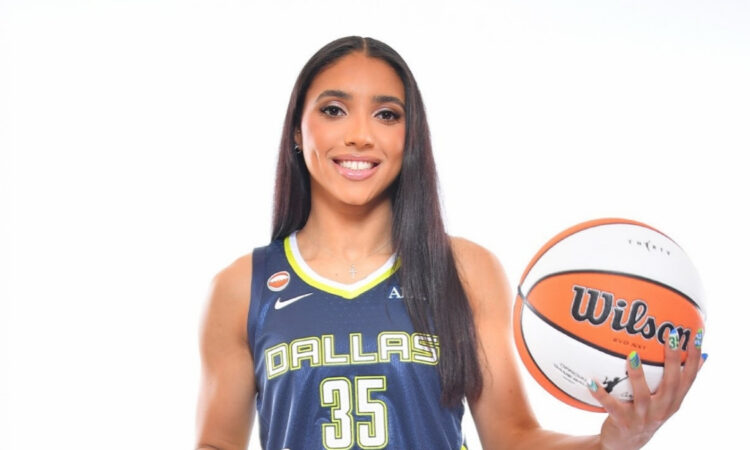 Azzi Fudd in a navy blue Dallas Wings Nike Explorer Edition jersey holding a basketball at her 2026 introductory press conference.