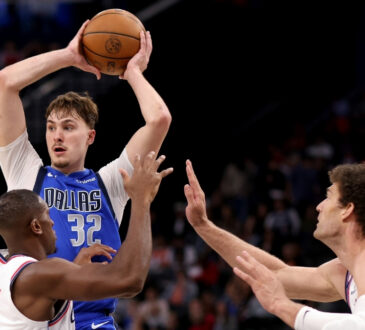 Cooper Flagg #32 of the Dallas Mavericks looks to pass while being guarded by Kris Dunn #8 and Brook Lopez #11 of the Los Angeles Clippers at Intuit Dome.