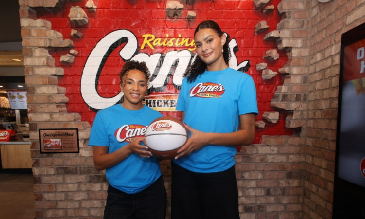 UCLA stars Lauren Betts and Kiki Rice posing with a basketball inside a Raising Cane’s restaurant in Hollywood after winning the 2026 NCAA Championship.