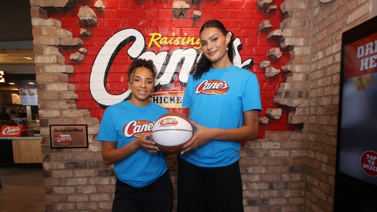 UCLA stars Lauren Betts and Kiki Rice posing with a basketball inside a Raising Cane’s restaurant in Hollywood after winning the 2026 NCAA Championship.