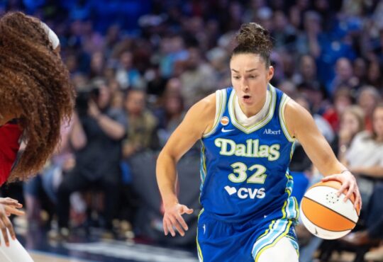 Jessica Shepard lowering her shoulder and dribbling the basketball with her right hand while driving past the tight perimeter defense of Kiki Iriafen.