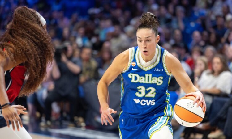Jessica Shepard lowering her shoulder and dribbling the basketball with her right hand while driving past the tight perimeter defense of Kiki Iriafen.