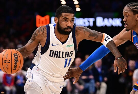 Guard Kyrie Irving wearing a blue Dallas Mavericks jersey while handling the ball on the perimeter against defender Jalen Williams of the Oklahoma City Thunder.