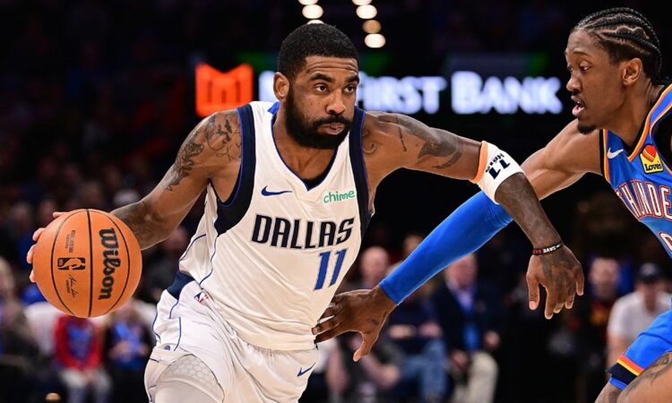 Guard Kyrie Irving wearing a blue Dallas Mavericks jersey while handling the ball on the perimeter against defender Jalen Williams of the Oklahoma City Thunder.
