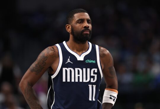 Guard Kyrie Irving wearing a white Dallas Mavericks jersey, looking on intently during a break in the action against the Denver Nuggets.
