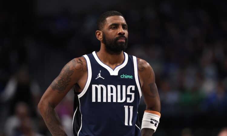Guard Kyrie Irving wearing a white Dallas Mavericks jersey, looking on intently during a break in the action against the Denver Nuggets.