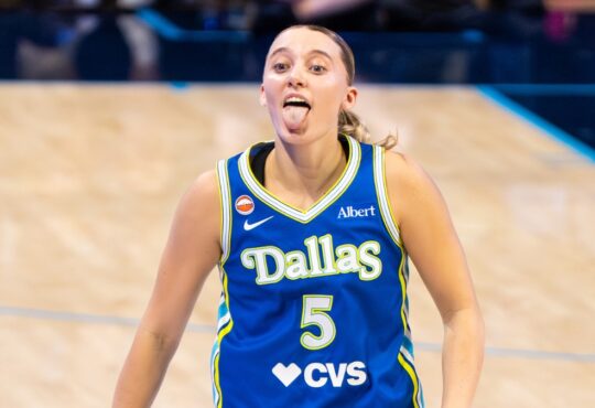 Guard Paige Bueckers celebrating on the court, smiling and gesturing dynamically after a successful offensive sequence.