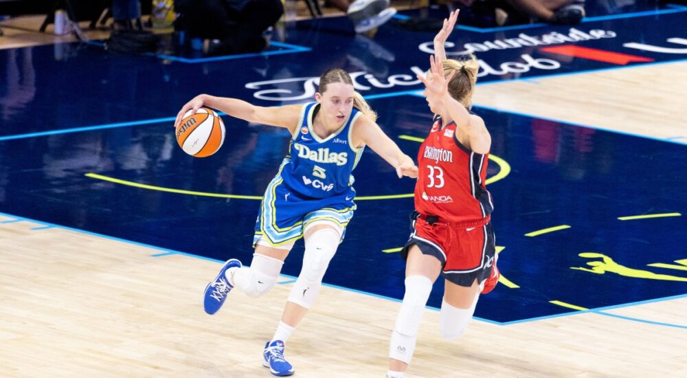 Paige Bueckers dribbling the basketball with her left hand while surveying the floor and advancing up the court under defensive pressure from Lucy Olsen.