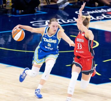 Paige Bueckers dribbling the basketball with her left hand while surveying the floor and advancing up the court under defensive pressure from Lucy Olsen.