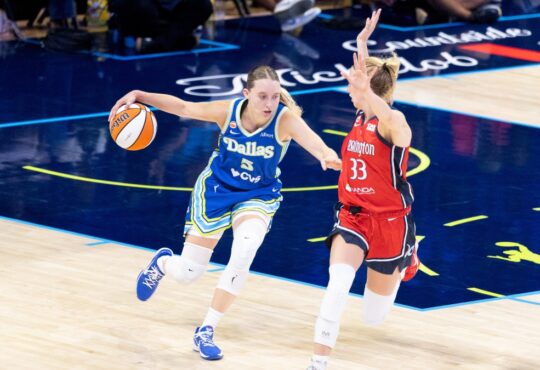 Paige Bueckers dribbling the basketball with her left hand while surveying the floor and advancing up the court under defensive pressure from Lucy Olsen.