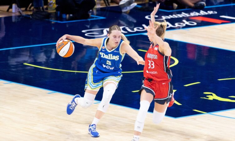 Paige Bueckers dribbling the basketball with her left hand while surveying the floor and advancing up the court under defensive pressure from Lucy Olsen.