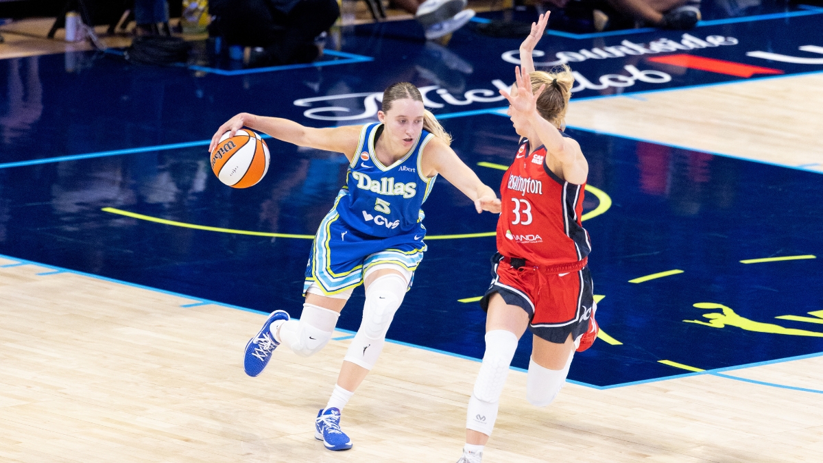 Paige Bueckers dribbling the basketball with her left hand while surveying the floor and advancing up the court under defensive pressure from Lucy Olsen.