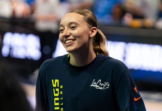 Guard Paige Bueckers wearing a blue Dallas Wings zip-up warmup jacket on the court before a game.