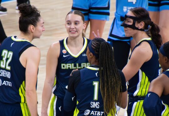 Jessica Shepard, Paige Bueckers, Alanna Smith, Odyssey Sims, and Arike Ogunbowale huddled tightly together on the court discussing a play during a timeout.
