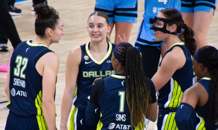 Jessica Shepard, Paige Bueckers, Alanna Smith, Odyssey Sims, and Arike Ogunbowale huddled tightly together on the court discussing a play during a timeout.