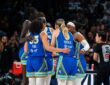 Dallas Wings players in blue road uniforms huddle together during a timeout against the Las Vegas Aces, with Azzi Fudd and Paige Bueckers visible from behind.