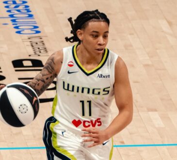 Dallas Wings guard JJ Quinerly dribbles up the court in a white No. 11 home jersey during a game against the Phoenix Mercury.