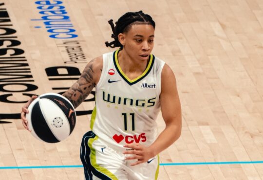 Dallas Wings guard JJ Quinerly dribbles up the court in a white No. 11 home jersey during a game against the Phoenix Mercury.
