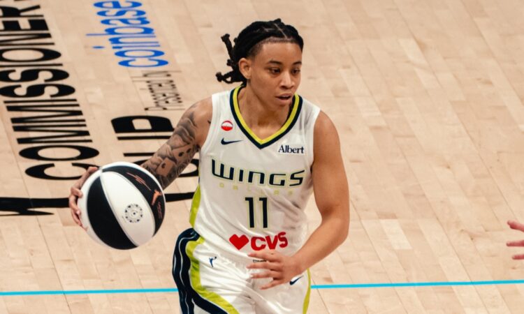 Dallas Wings guard JJ Quinerly dribbles up the court in a white No. 11 home jersey during a game against the Phoenix Mercury.