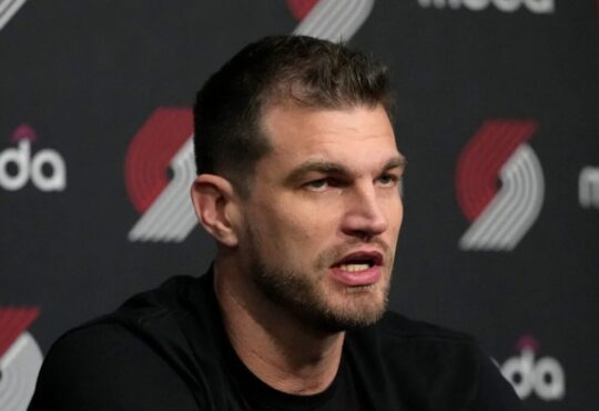 Tiago Splitter speaking at a Portland Trail Blazers press conference in front of a Moda and Trail Blazers logo backdrop