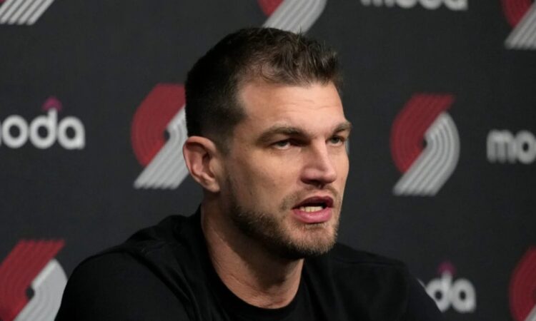 Tiago Splitter speaking at a Portland Trail Blazers press conference in front of a Moda and Trail Blazers logo backdrop