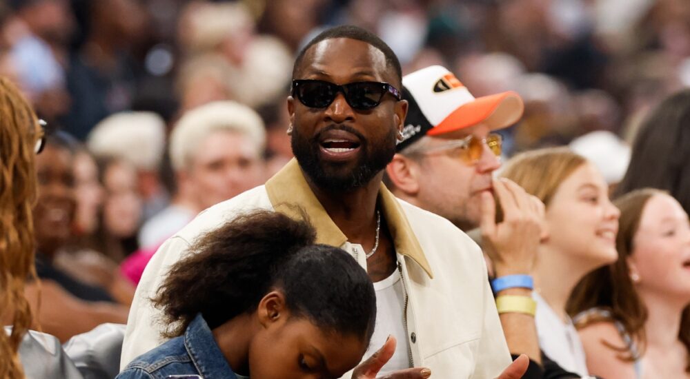 Dwyane Wade sits courtside in sunglasses and a cream jacket during the 2026 WNBA All-Star Game at United Center in Chicago.