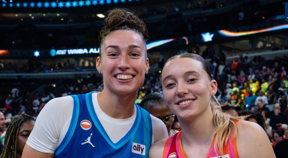 Jessica Shepard, in a blue Team Spoon jersey, and Paige Bueckers, in an orange Team Coop jersey, stand together and smile on the court after the 2026 WNBA All-Star Game.