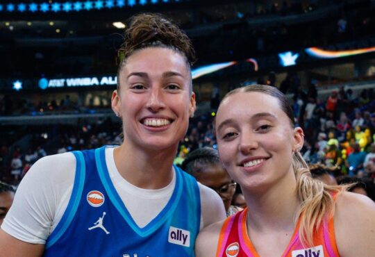 Jessica Shepard, in a blue Team Spoon jersey, and Paige Bueckers, in an orange Team Coop jersey, stand together and smile on the court after the 2026 WNBA All-Star Game.
